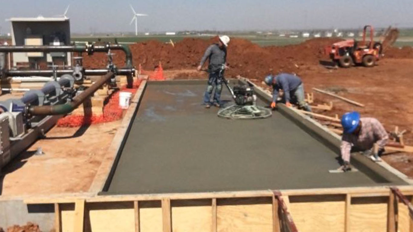 3 men smoothing out a pad of concrete for a pipeline facility